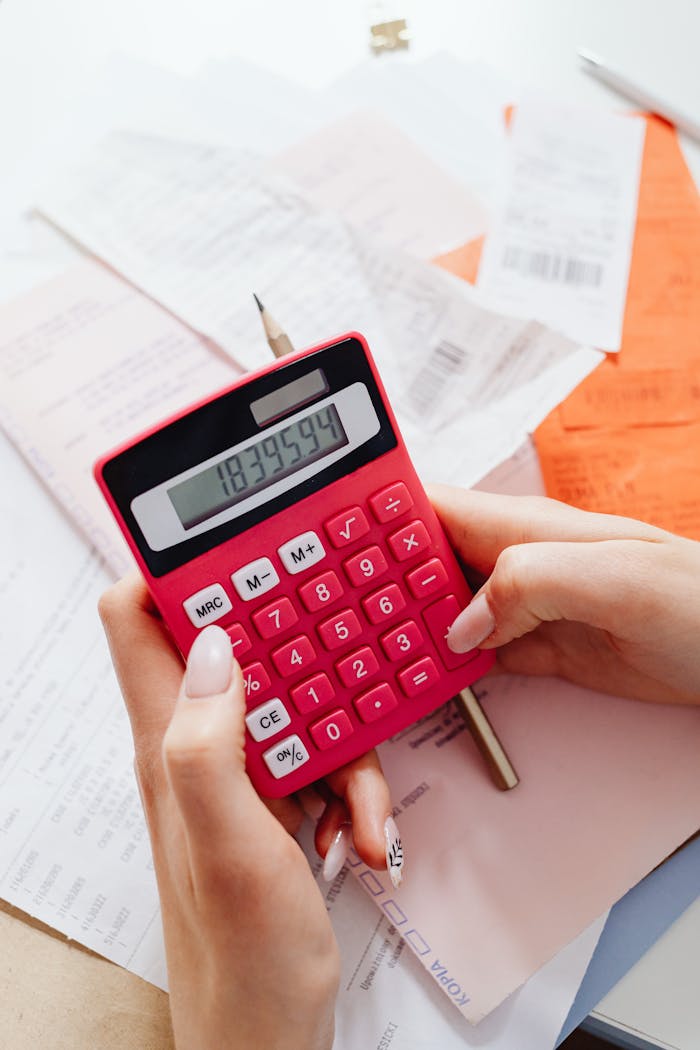 A person calculating finances on a red calculator surrounded by documents.